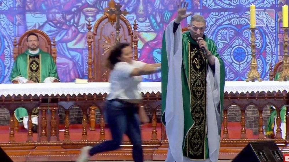 Una mujer empuja a un sacerdote anti-gay megafamoso fuera del escenario frente a 50.000 católicos rezando 1