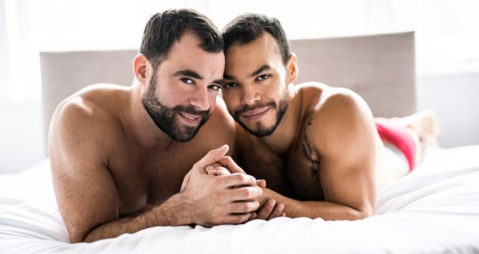 Two men in bed together, holding hands