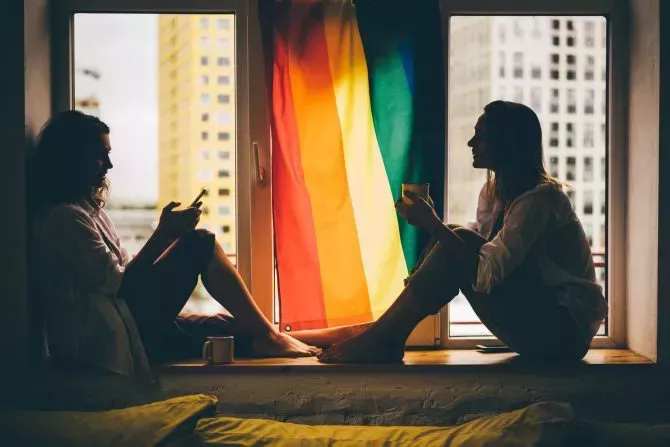 Lesbian couple in love sitting near the window with the rainbow flag