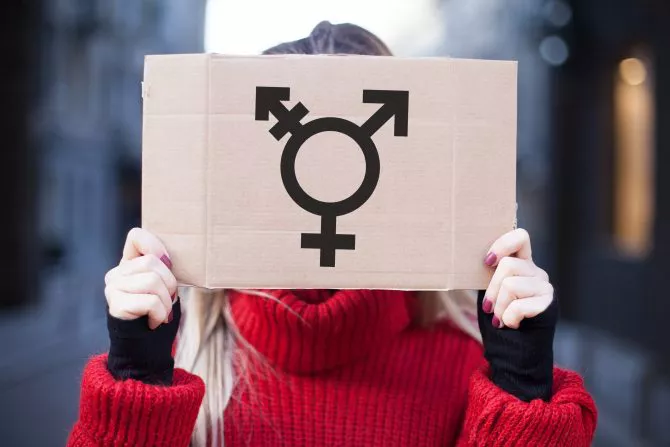The symbol of the transgender in hands on a cardboard plate, covering the face
