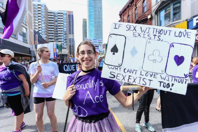 ASEXUALS march, holding IF SEX EXISTS WITHOUT LOVE, WHY CAN'T LOVE EXIST WITHOUT SEX sign
