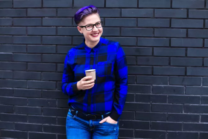 Portrait of cute beautiful young lesbian with short haircut and trendy boyish clothes drinking cup of coffee