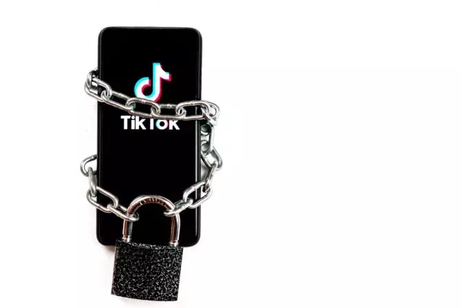Tiktok logo on a smartphone. The telephone is tied with an iron chain and has a large padlock on it.
