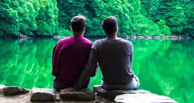 Two gay men sit by a lake