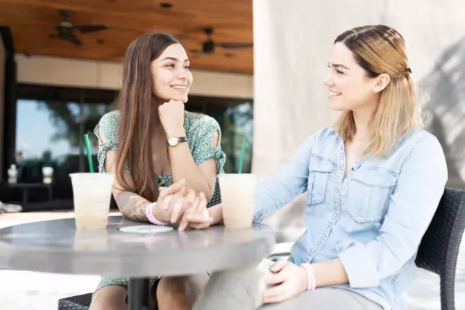 cute lesbian couple sitting outside a coffee shop holding hands, talking and drinking latte