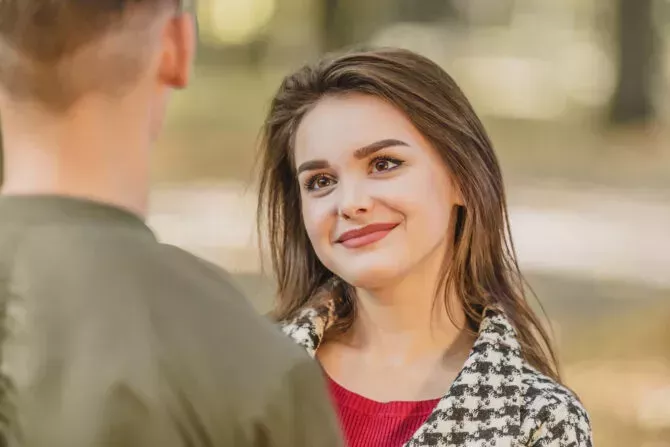 Adorable young woman is looking at her boyfriend, standing back to the camera, with big admiration and appreciation.