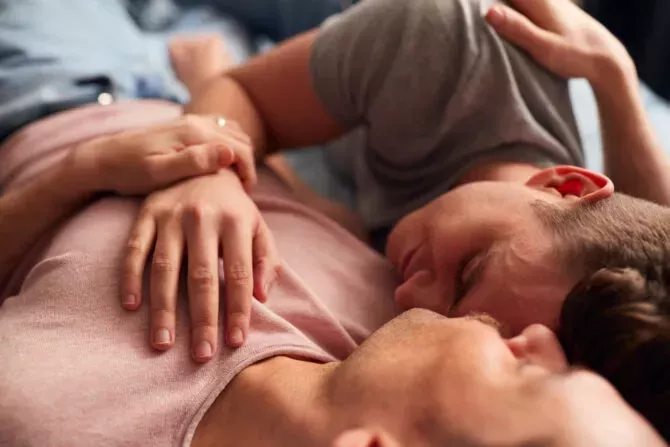 Close Up Shot Of Loving Same Sex Male Couple Lying On Bed At Home Hugging Together