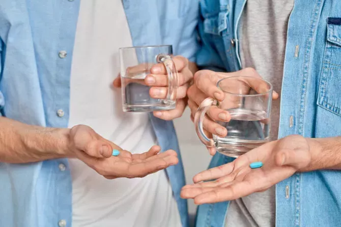 Cropped view of gay couple holding mug with water and pre exposure HIV protection pills in hands