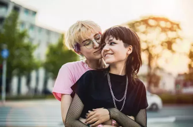 Young gender fluid couple hugging on city street