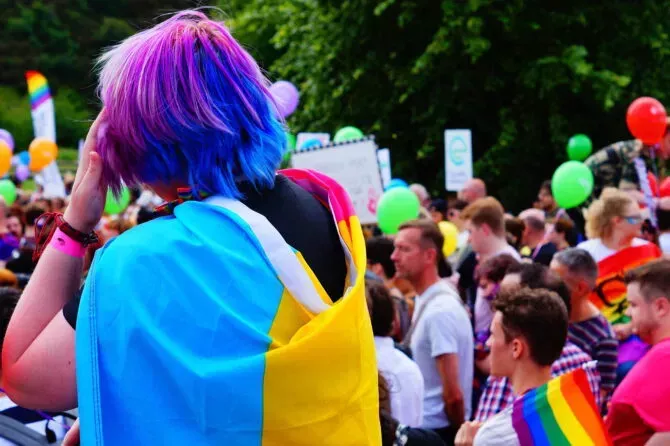 Young person with colored hair and pansexual pride flag around shoulders at Edinburgh Pride March
