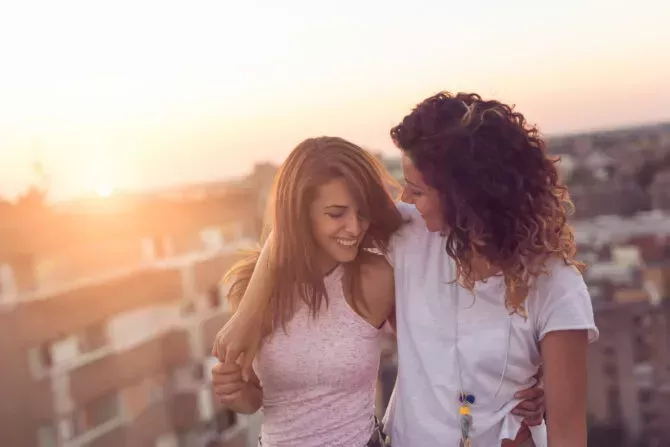 Lesbian couple standing and hugging on a building roof at sunset