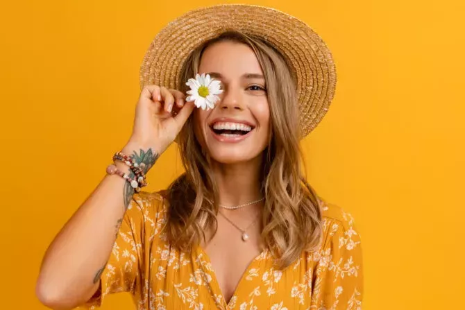 stylish woman in yellow dress and straw hat holding daisy flower