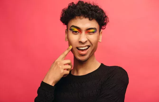 Gay man wearing multicolored shadows on eyelids blinking at camera