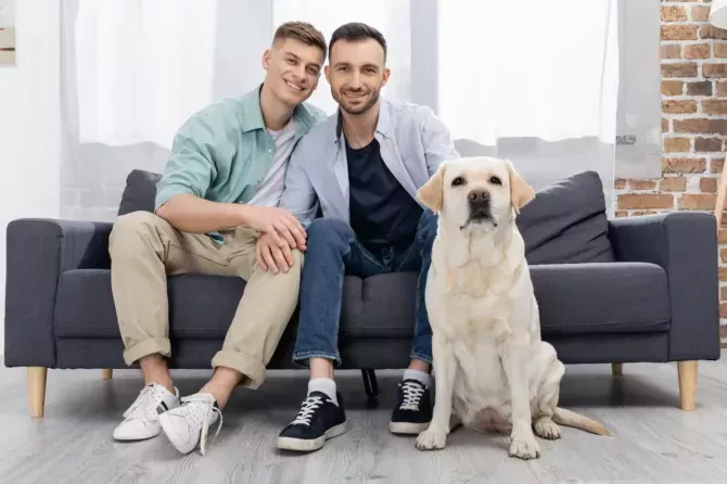 same sex couple sitting on sofa near dog in living room