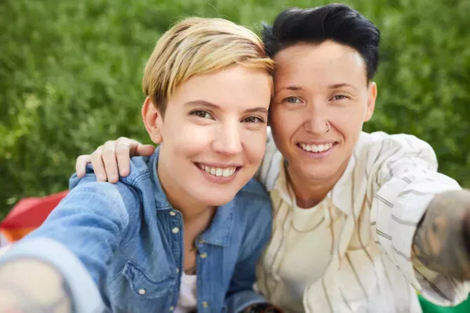 Portrait of two happy lesbians smiling at camera they taking selfie portrait while sitting outdoors