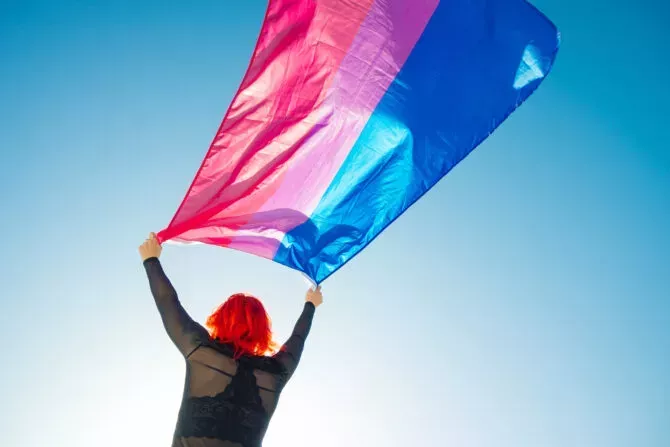 Woman holding the Bisexual Rainbow Flag with the blue sky in the background