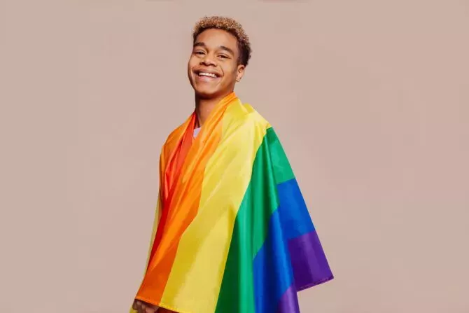 Portrait of happy smiling afro latin american young man with a gay pride rainbow flag at studio over beige background