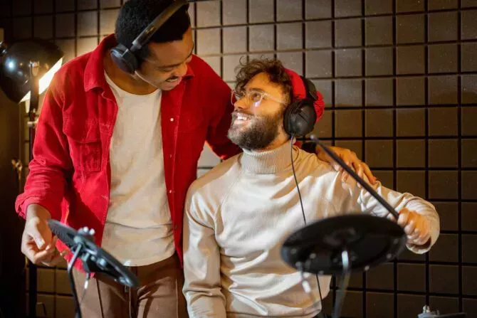 Two male close friends hug while playing electric drums