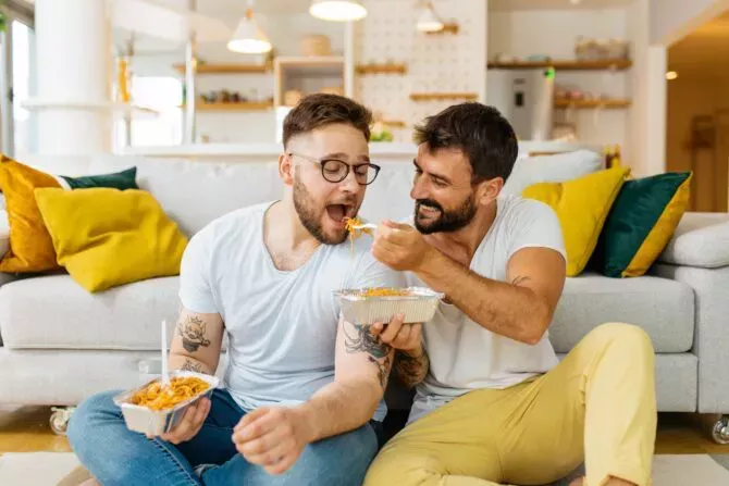 married hipster couple sitting on the floor in the living room and eating pasta for dinner