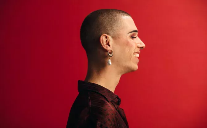 Profile view of androgynous man wearing an earring and makeup smiling