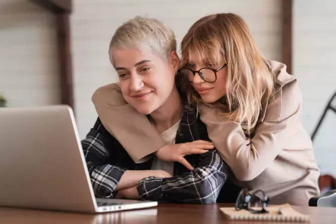 Lesbian couple embracing while looking at a laptop