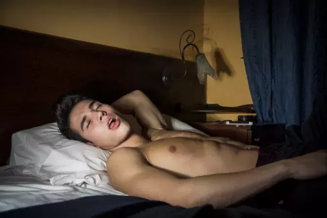 Handsome shirtless athletic young man laying in bed at night with eyes closed, sleeping