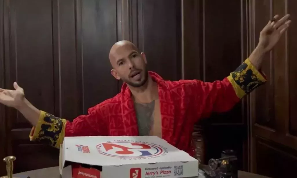 Andrew Tate gestures with both hands in the air while pizza boxes are seen in front of him