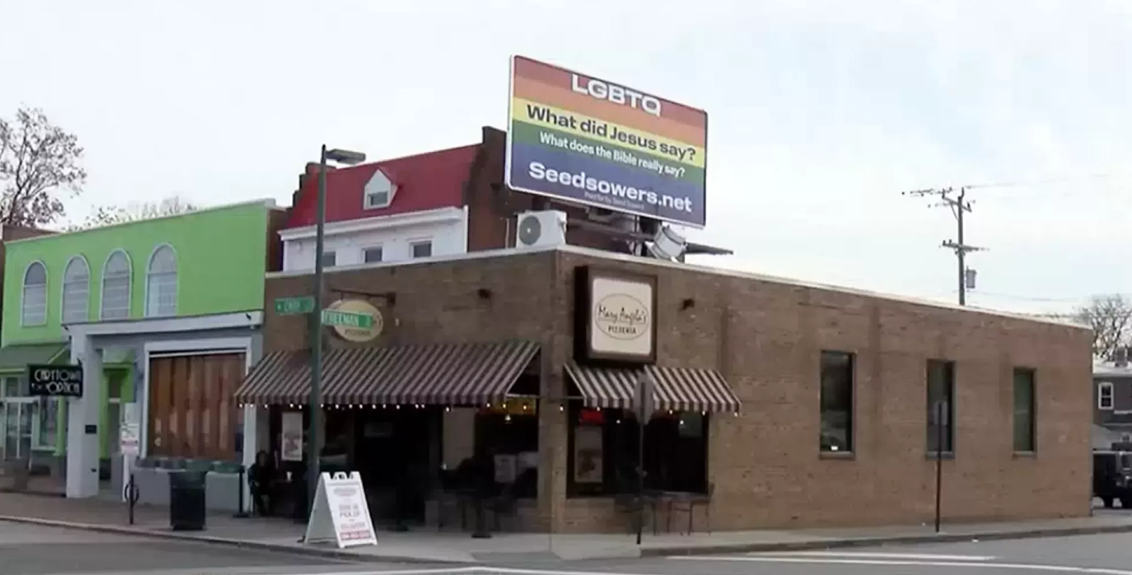 A rainbow colored billboard with heavily Christian text sits atop Mary Angela's Pizzeria in Carytown, Virginia.