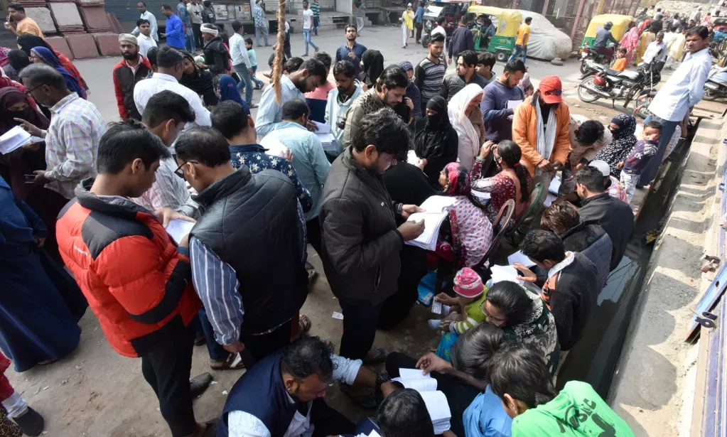 A group of people stand around in a local street, getting read to vote in the MCD elections