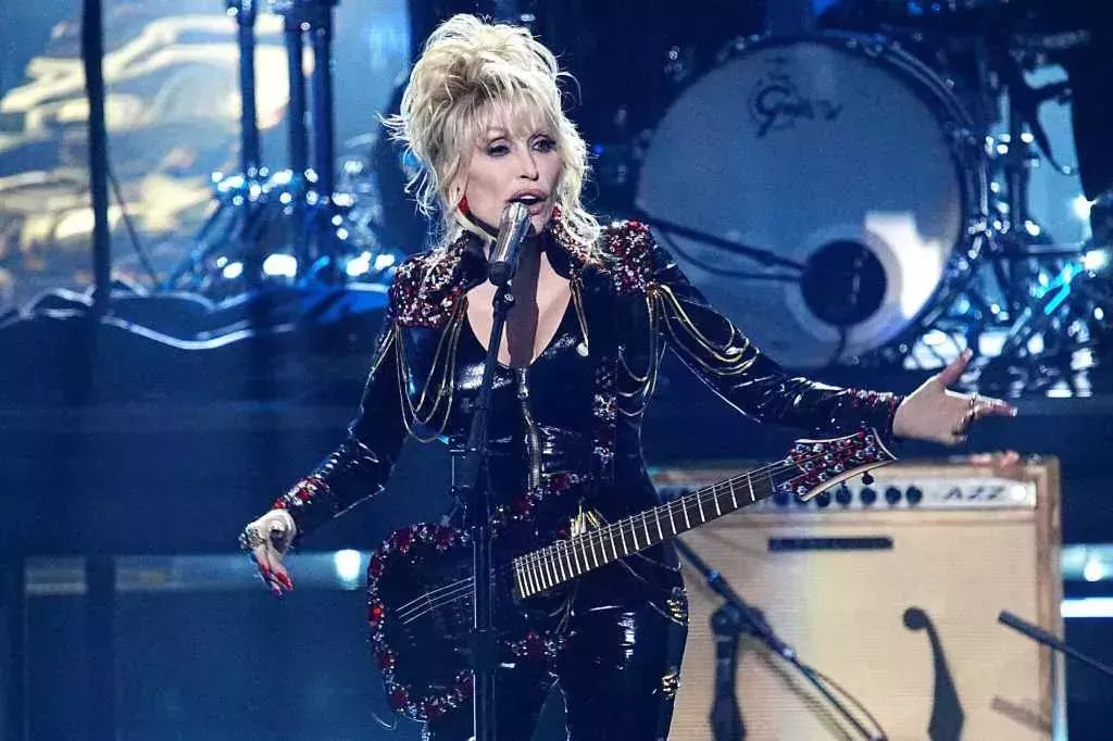 Dolly Parton, wearing a black leather outfit, performs on stage with a black electric guitar during the 37th Annual Rock & Roll Hall Of Fame Induction Ceremony.
