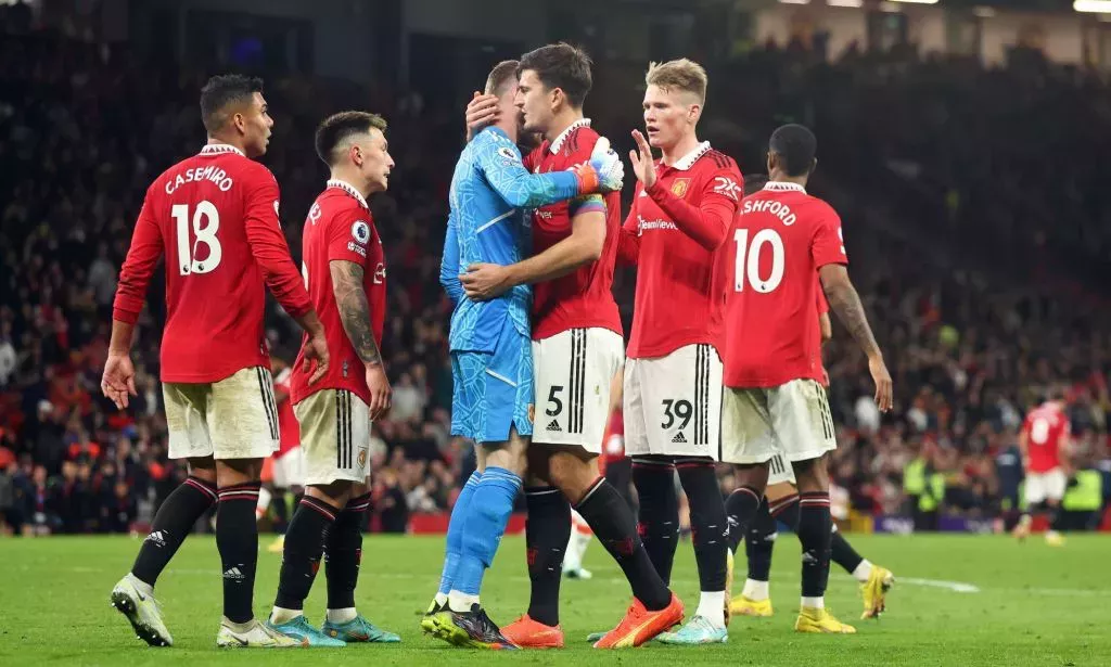 Manchester United players, wearing red football uniforms, gather around each other