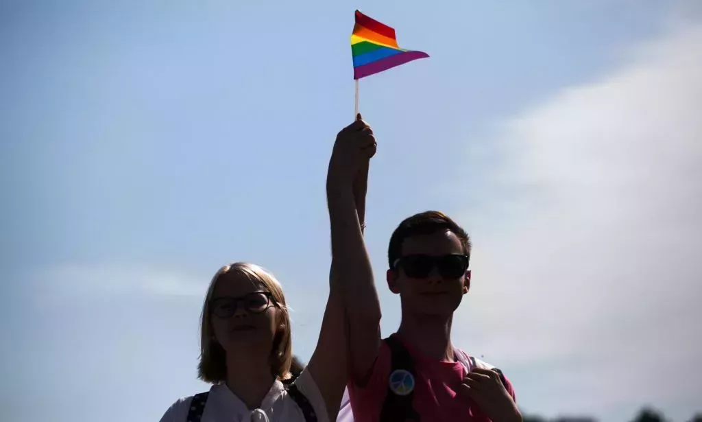 Two people stand side-by-side as they hold up a rainbow LGBTQ+ Pride flag together during a protest in Russia