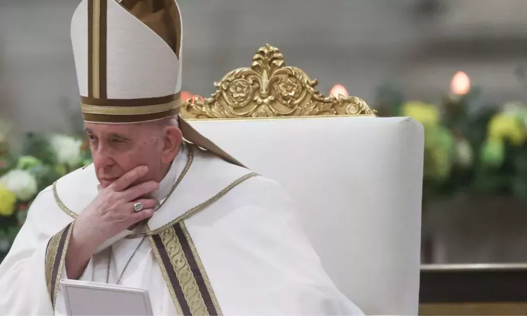 Pope Francis wears white garments while he sits on a white and gold chair during a mass