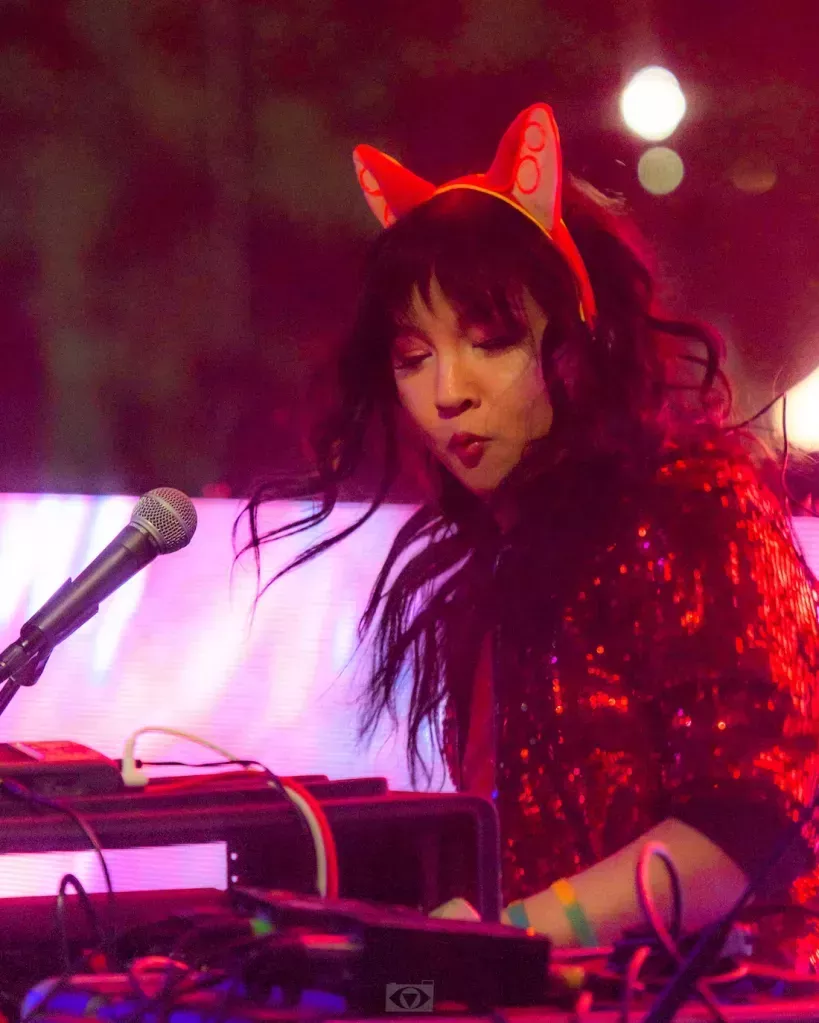 EDM artist Freya Fox on stage wearing bunny ears standing at a microphone. She is wearing a red outfit.
