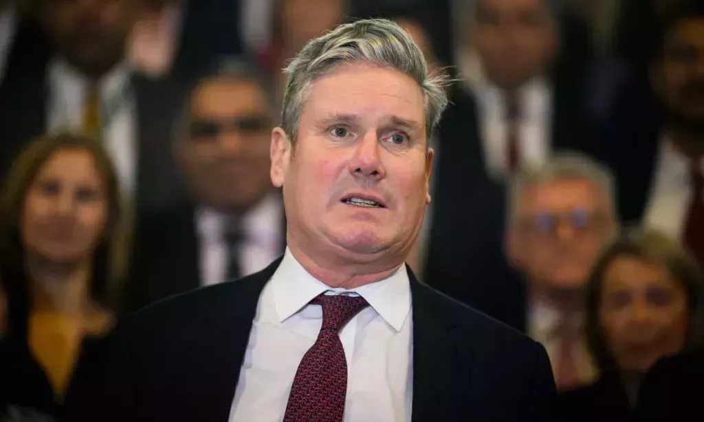 Keir Starmer, wearing a dark red tie, speaks in front of a group of people.