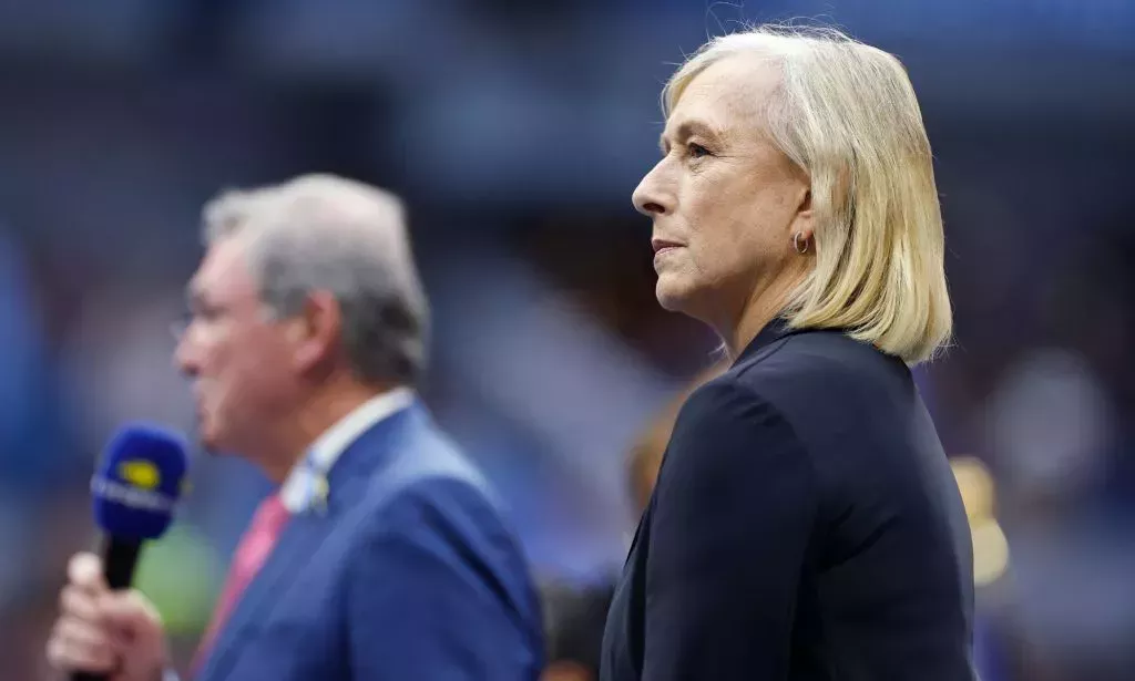 Martina Navratilova standing in a Tennis court, next to an individual wearing a blue blazer and holding a microphone.