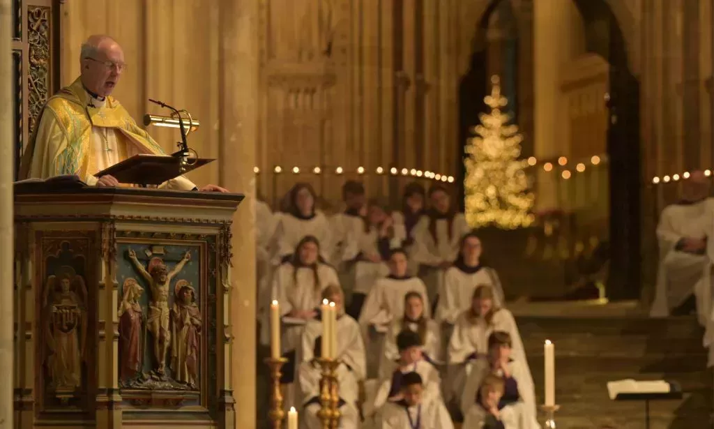 The Archbishop of Canterbury sings on a pedestal as a group of Christians stand beside him.