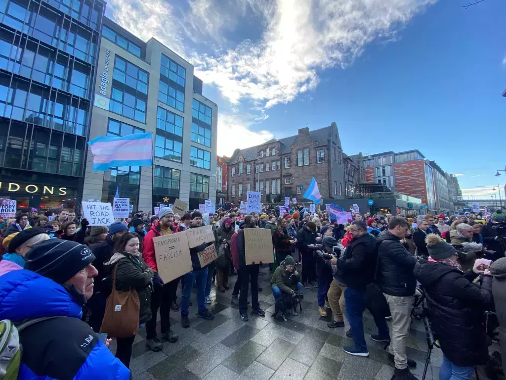 A photo shows trans activists standing in edinburgh for a trans rights rally. Some are holding signs