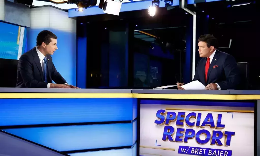 Pete Buttigieg speaks to Brett Bair over a blue LED table on a Fox News set