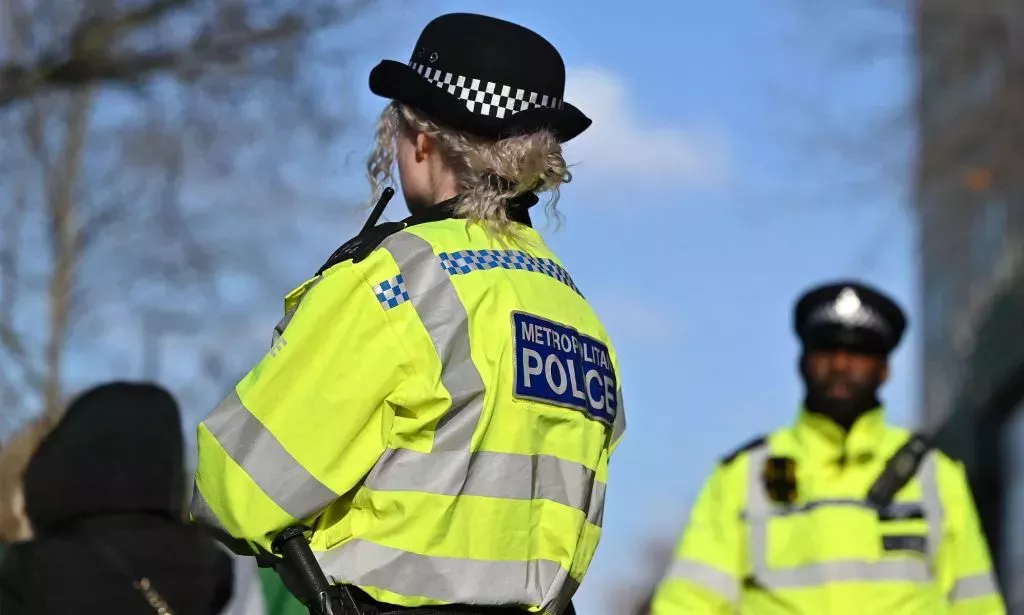 Two Met Police officers, wearing high vis jackets, stand outside.
