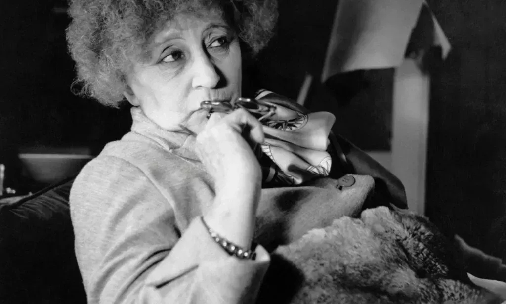 French author Colette poses with a hand near her mouth in a black and white photo