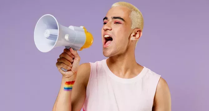 A queer man in makeup shouts through a loudspeaker