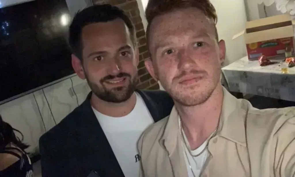 Ricardo and Bradleigh, a gay couple, wear white shirts and other shirts on top as they stare at the camera while being indoors