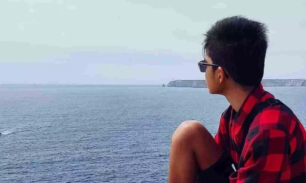 Rayyan Aboobaker, an ambassador for LGBTQ+ youth charity Just Like Us, wears a red and black plaid shirt as he sits with his back to the camera