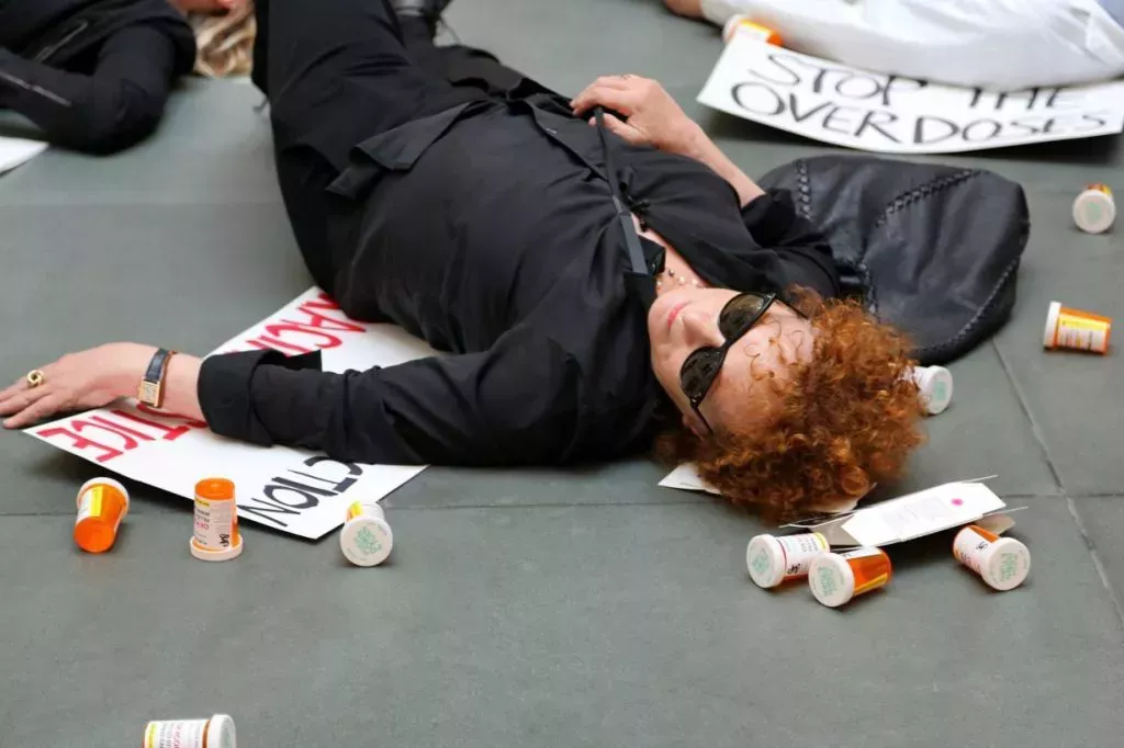 Nan Goldin at a demonstration, pretending to be passed out surrounded by opioid bottles