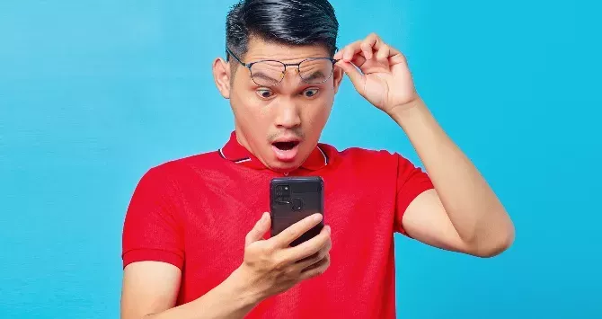 A man looks with shock and surprise at his cellphone