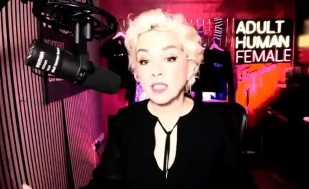 Kellie-Jay Keen, also known as Posie Parker, speaks into a microphone with a black-and-pink background