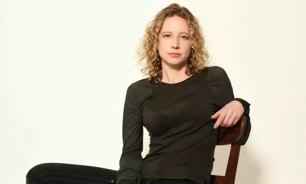 Queer stunt driver and professional drift driver Zandara Kennedy wears a black outfit as she sits in a chair and poses for the camera