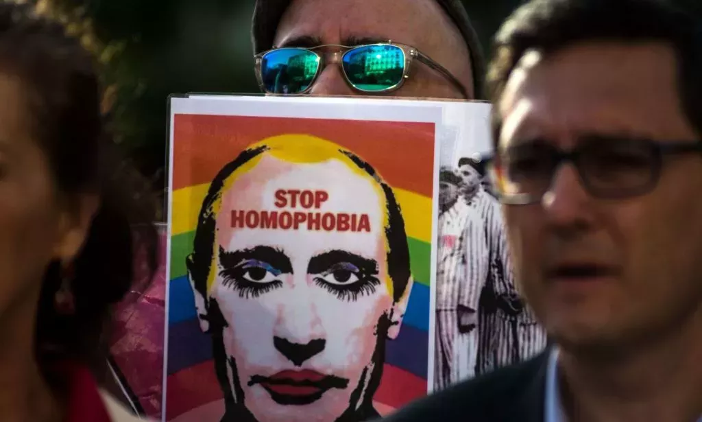 A person holds up a sign with the face of Russia's president Vladimir Putin with an LGBTQ+ rainbow flag in the background and words 'stop homophobia' on it as Putin's government increasingly attacks queer people and labels LGBTQ+ rights groups as 'foreign agents'