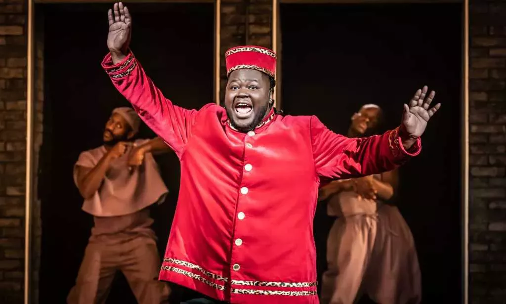 Kyle as Usher, a fat Black man wearing a red theatre usher costume